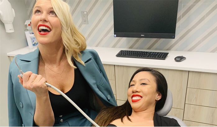 Dr. Alterman squirts a water sprayer at the new office's grand opening. Dr. Tran looks on, reclined in treatment chair. Both laugh.